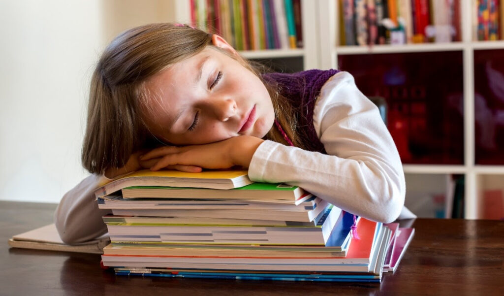 A young school girl sleeping on her textbooks.
